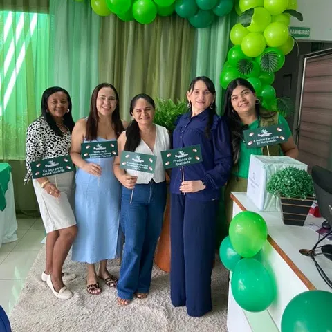 Mulheres sorriem sob um arco de balões verdes, com plaquinhas da Essencial Pharma.