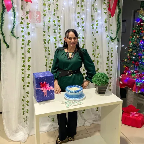 Uma mulher de vestido verde atrás de uma mesa com bolo e presentes, numa decoração de Natal.